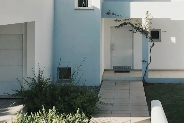 Paved approach and entry path running beside a rendered house wall.