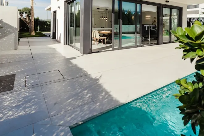 Pale large-format stone deck running the length of a swimming pool.
