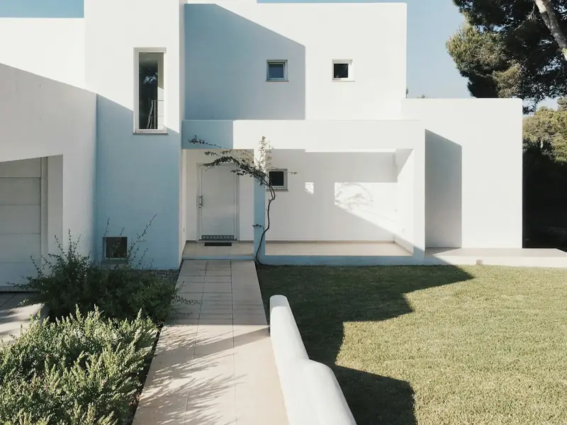 Paved path running between a planted border and a lawn beside a white stucco house.