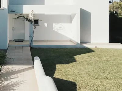 A low white rendered wall dividing a paved strip from a lawn, below a deep shaded opening.
