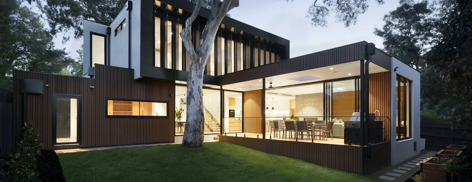 Covered terrace with a dining setting opening onto a level lawn at dusk.